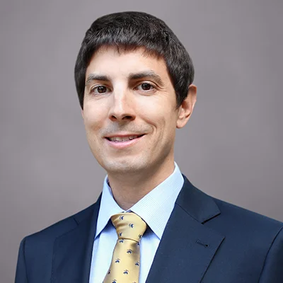 A headshot of Anthony Pizzo, a Senior Trader at SEIA, wearing a navy blue suit, light blue button-down shirt, and yellow tie with small blue flowers.