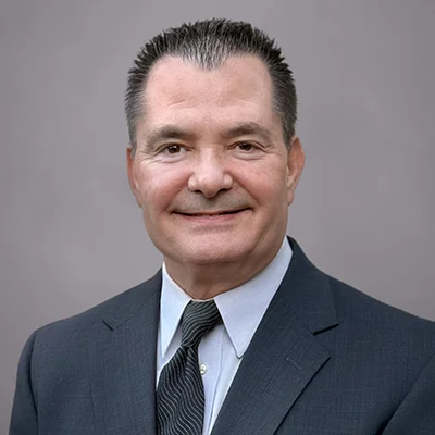 A headshot of John Barrick, a Senior Client Service Associate at SEIA, wearing a blue-gray suit, light blue button-down shirt, and dark blue tie.